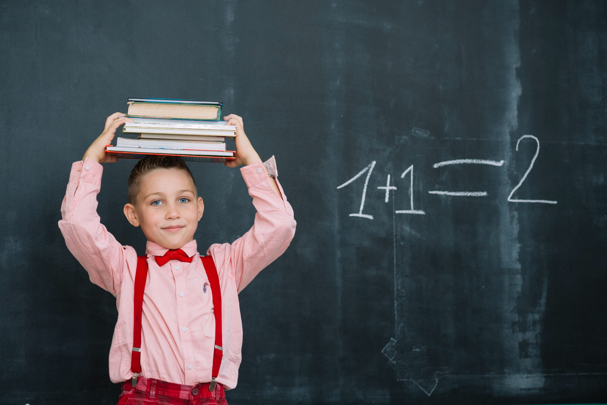 Menino com livros na cabeça efetuando adição com material dourado no 2º ano